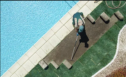 A man using a shovel to work on a pool, focused on his task in a sunny outdoor setting.